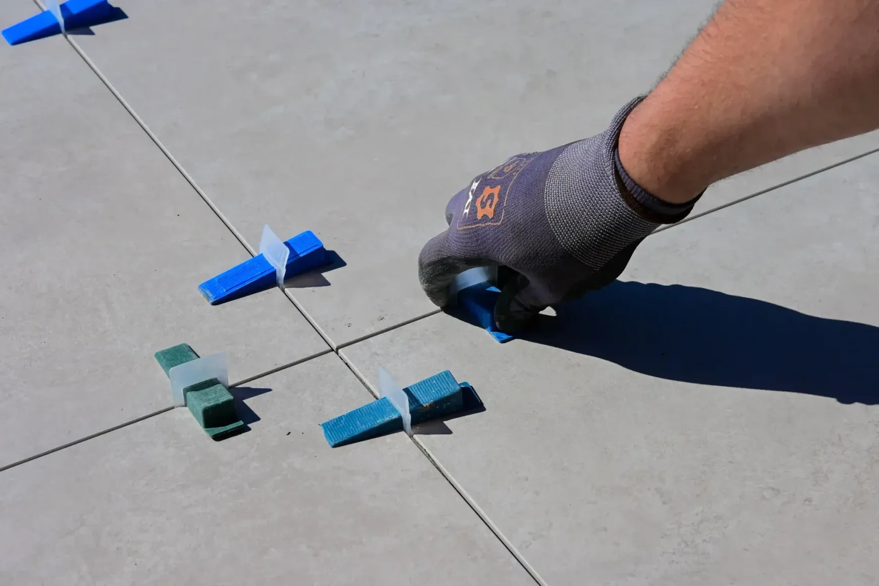 Tile installer placing leveling clips and wedges between large-format floor tiles