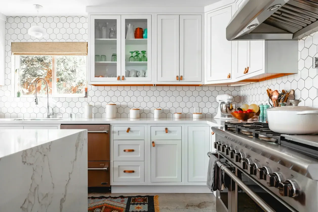 White hexagon tile backsplash behind shaker cabinets with leather pulls and professional range